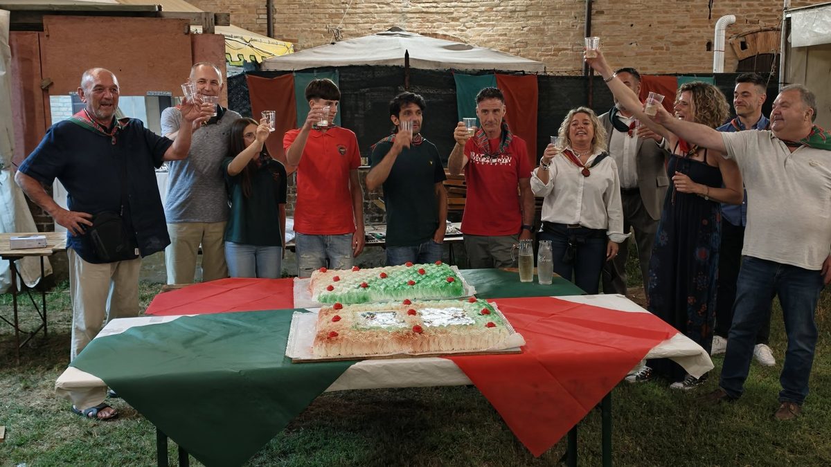 Contradaioli brindano attorno a due torte su un tavolo con il drappo rosso e verde